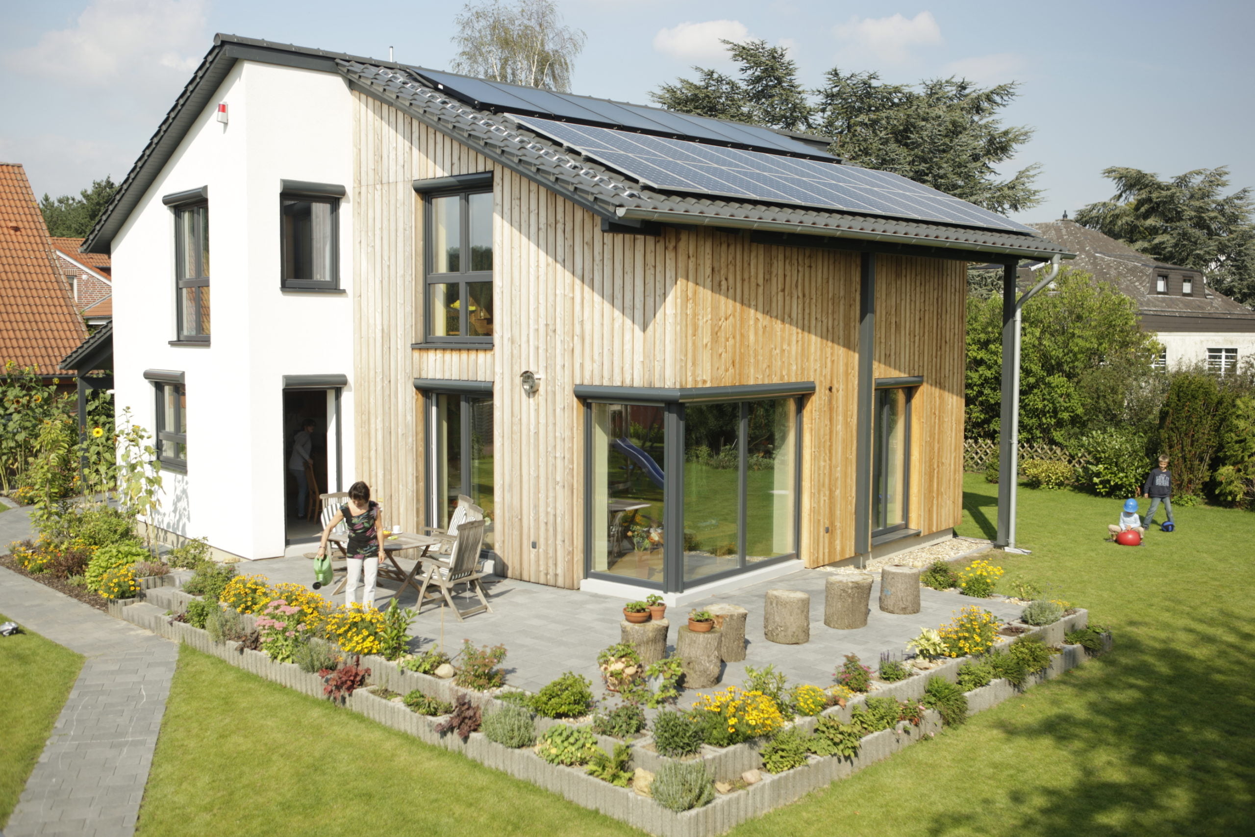Ein Plus-Energiehaus Neubau von wohnbehagen mit weißer und hölzener Fassade auf grünem Grundstück.