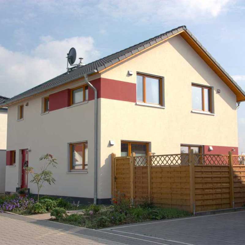 Einfamilienhaus Effi 55 mit Vorgarten, eingezäuntem Garten und roten Akzenten an der Hauswand.