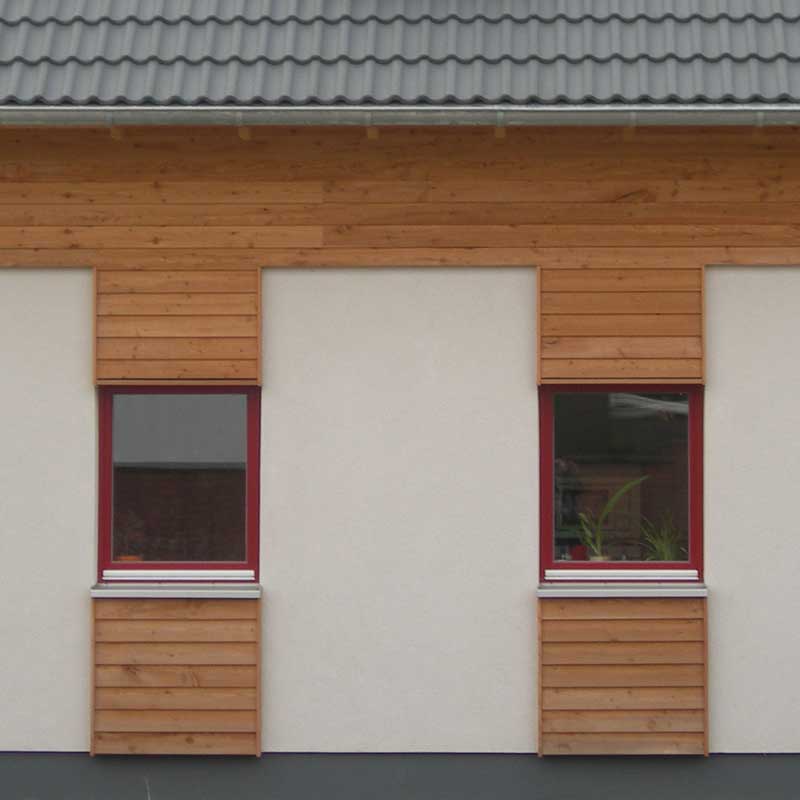 Zwei Fenster mit einem roten Rahmen und eine hölzerne Verkleidung über und unter den Fenstern.