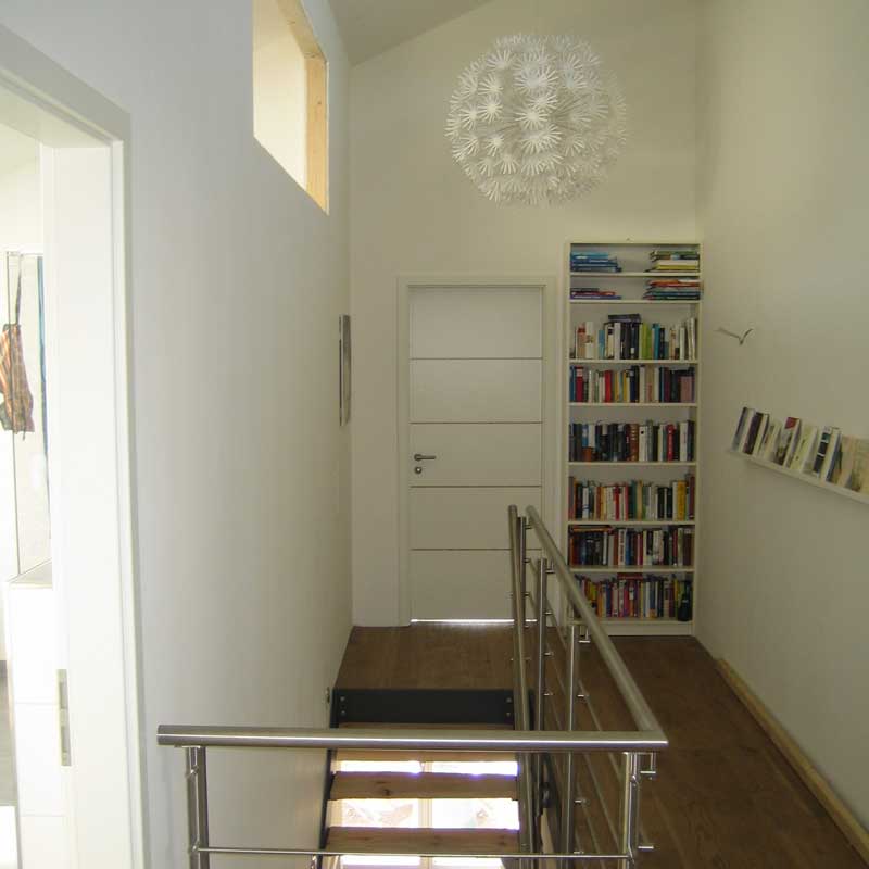 Ein Flur mit einer Treppe, die ins Erdgeschoss führt und einem Bücherregal in der rechten Ecke.