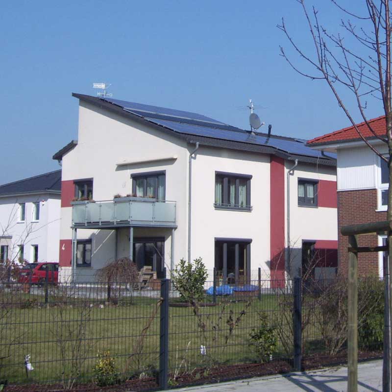 Ein Passivhaus mit 2 Wohneinheiten, einem Balkon, einer Terrasse und roten Akzenten an der Fassade.