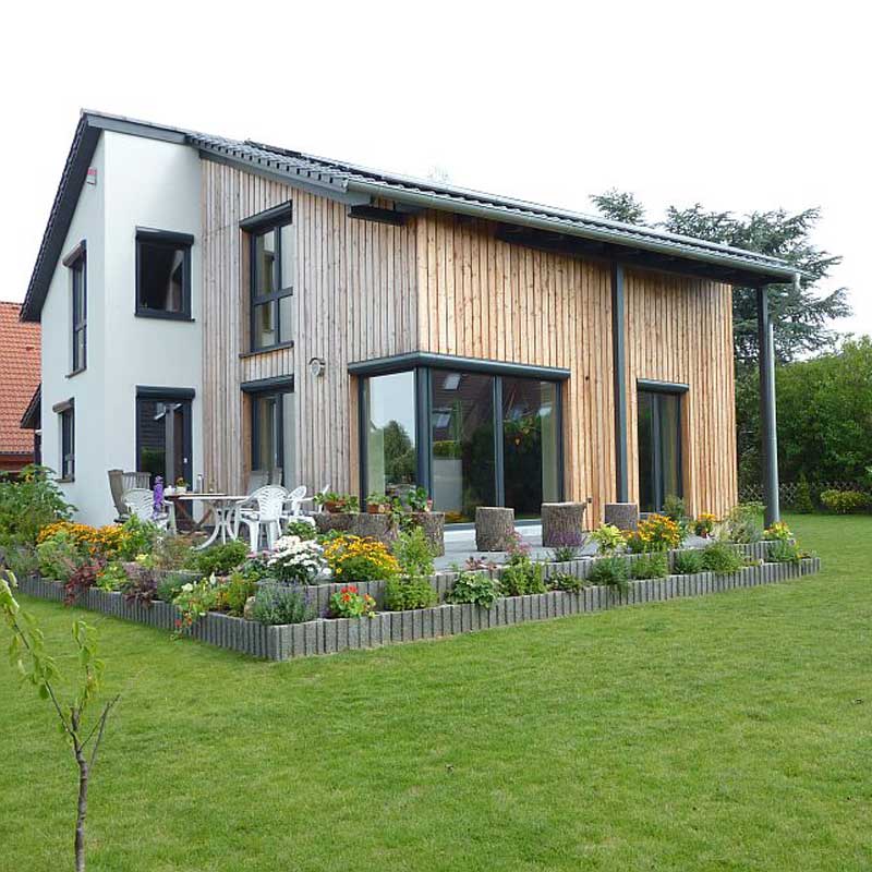 Ein Plus-Energiehaus von Wohnbehagen mit teils weißer, teils hölzener Fassade und einer Terrasse.