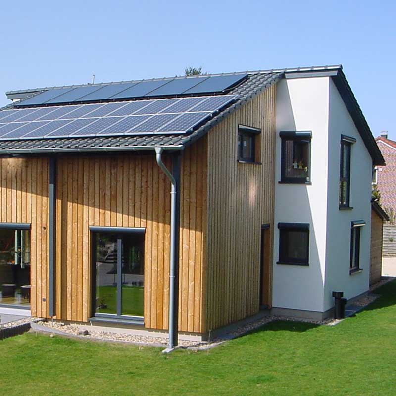 Ein Plus-Energiehaus von Wohnbehagen mit einem grauen Solardach auf der hölzenern Fassadenhälfte.