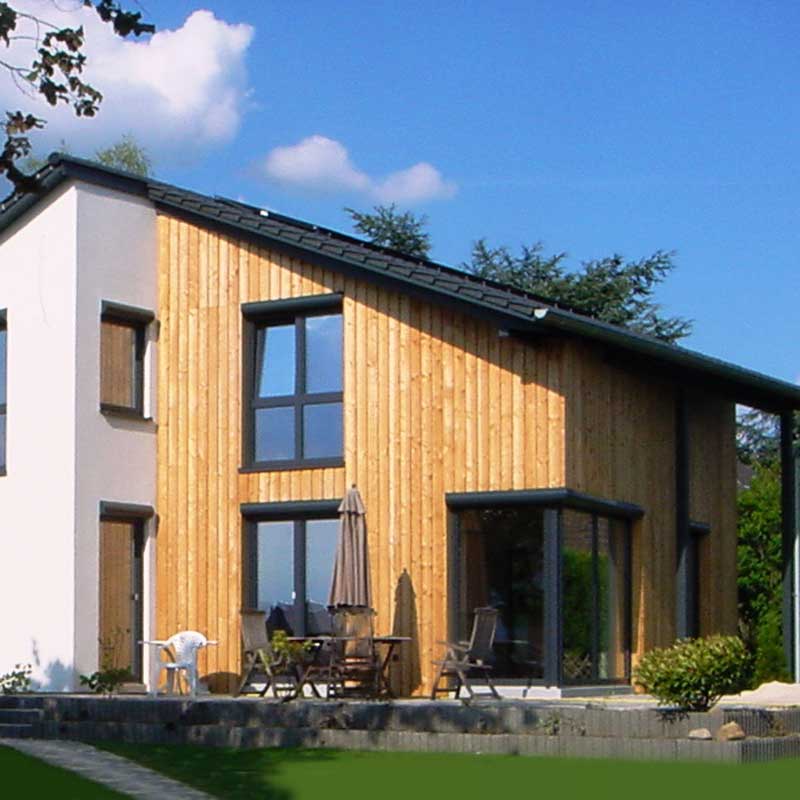 Ein Plus-Energiehaus von Wohnbehagen mit großen Fenstern und einer möblierten Terrasse.