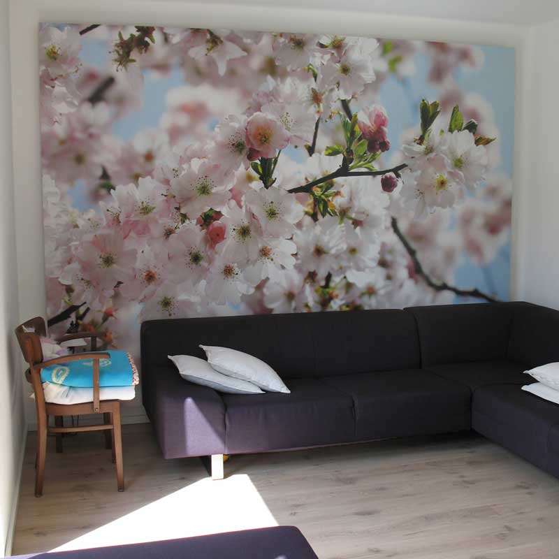 Eine Dunkellila farbige Eck-Couch und ein Stuhl vor einem großen Bild mit einem Kirschblütenmotiv.