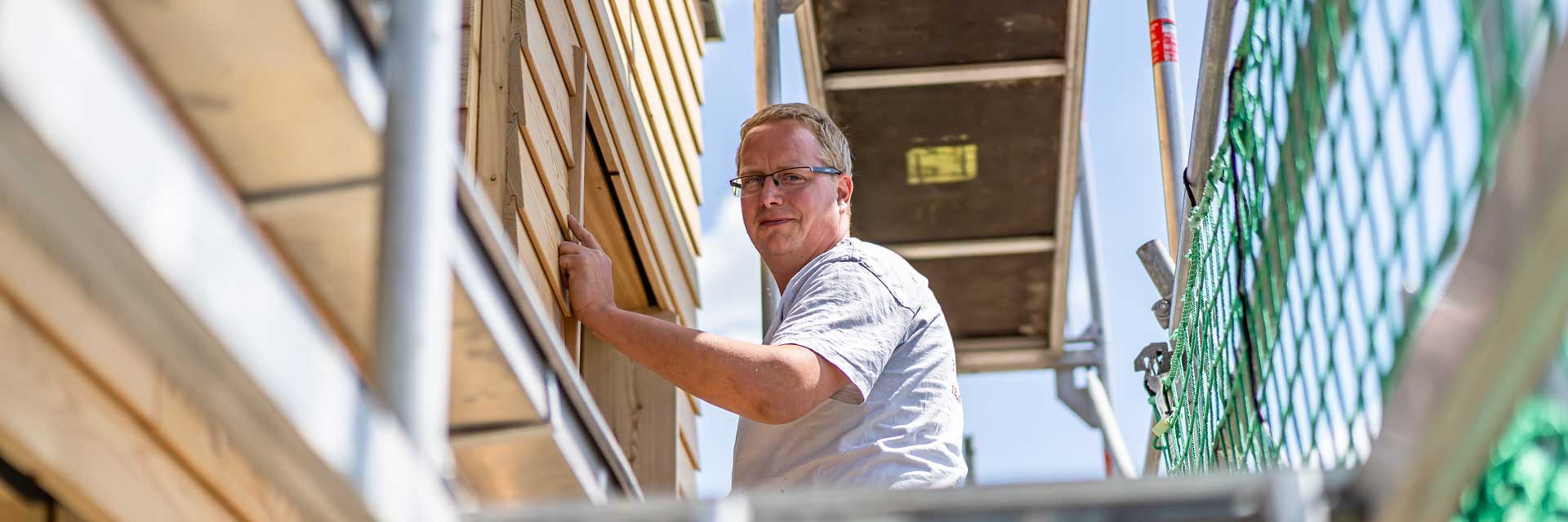 Ein Mitarbeiter arbeitet an der Holzfassade.