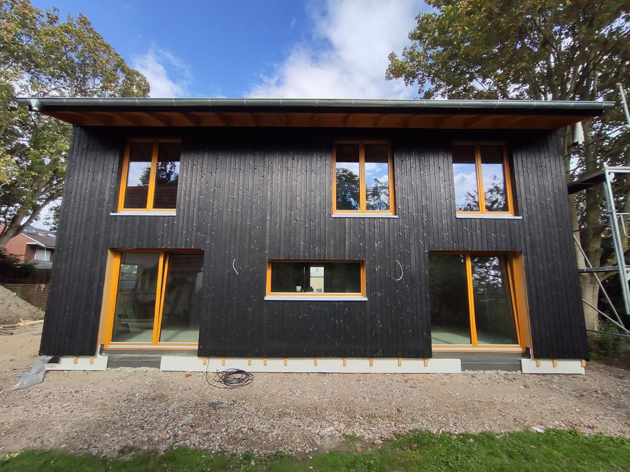 Ein Holzhaus von Wohnbehagen mit einer dunkelgrauen Holzvertäfelung und naturfarbenen Holzfenstern.