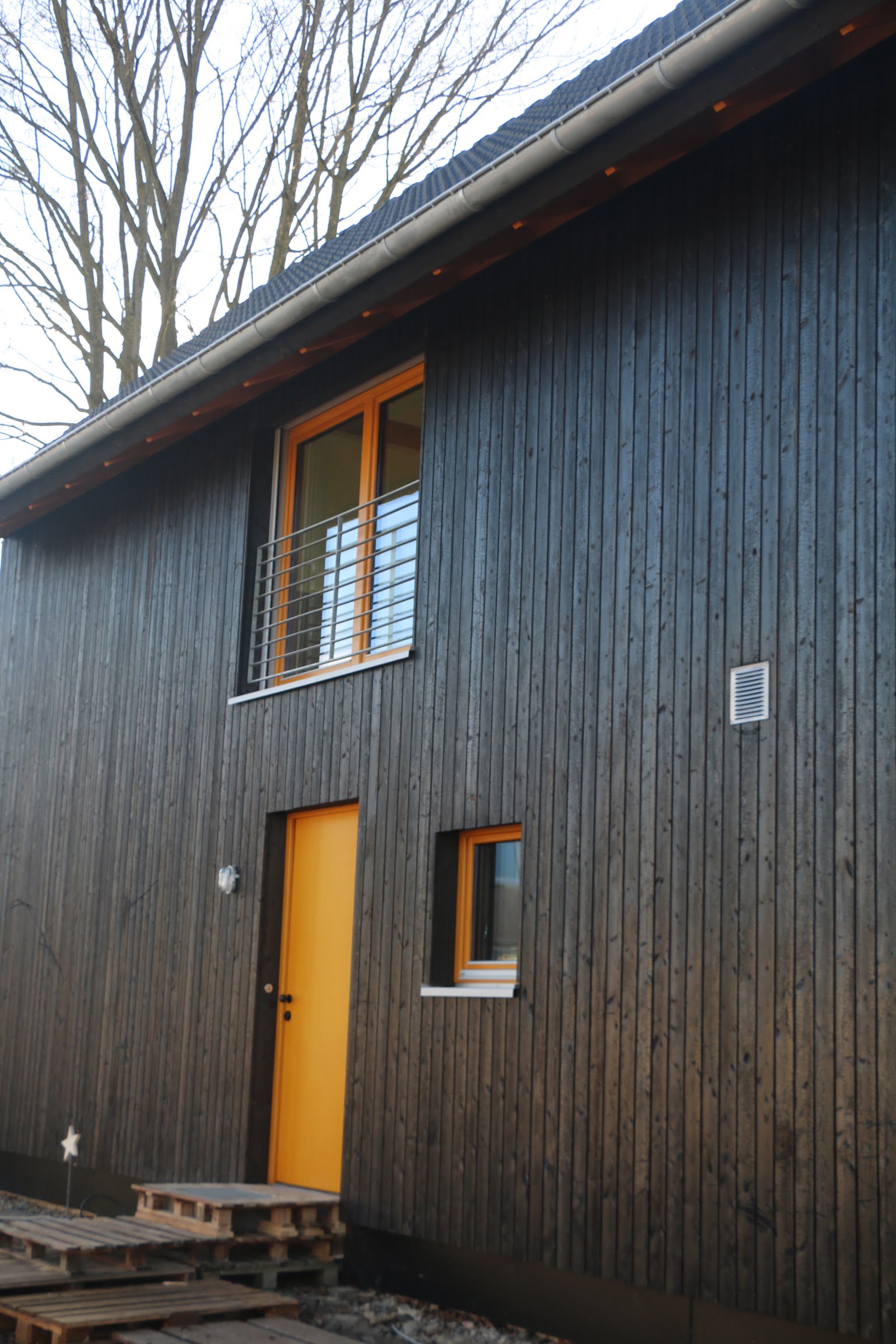 Eingang eines Holzhauses von Wohnbehagen mit einer dunklen Fassade und einer naturfarbenen Haustür.