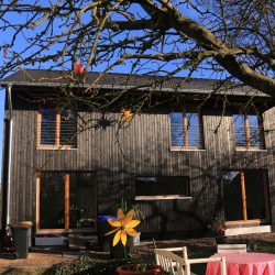 Ein Holzhaus von Wohnbehagen mit dunkelgrauer Holzvertäfelung an der Außenwand.