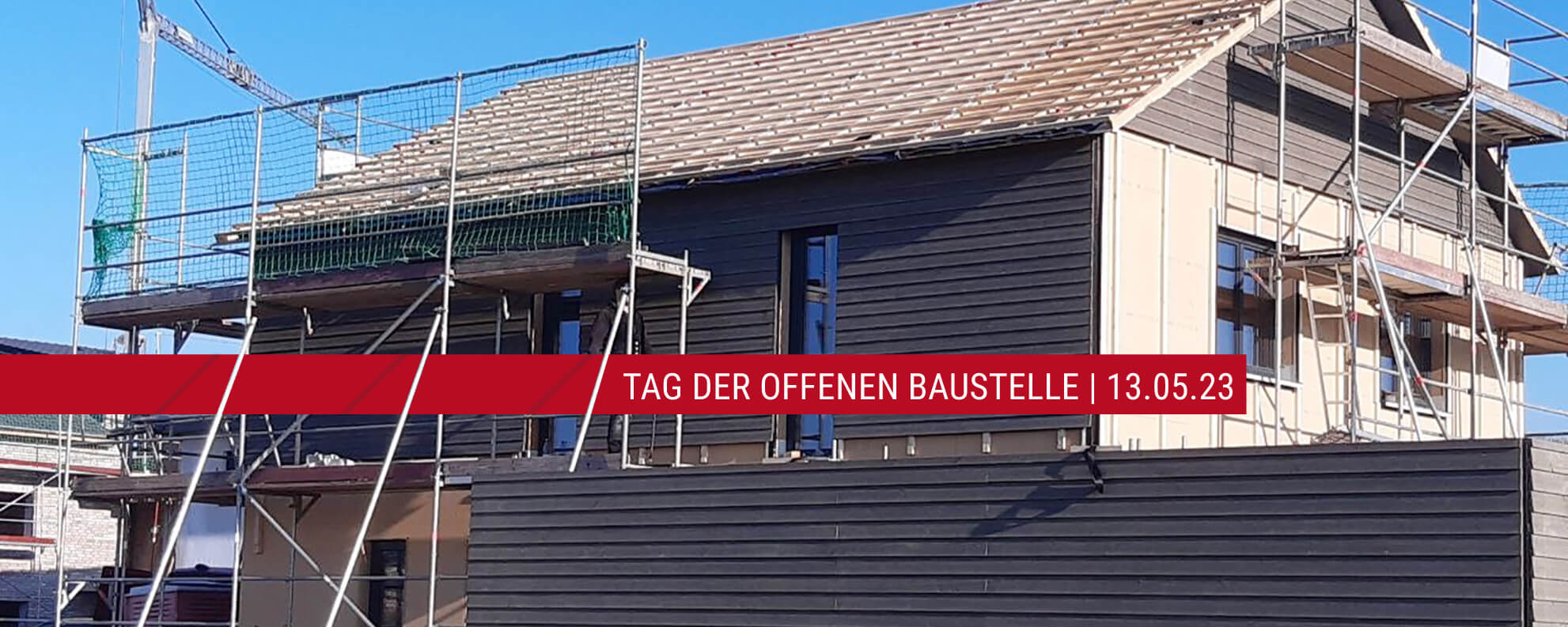 Ein unfertiges Holzfertighaus mit Baugerüsten lädt zum Tag der offenen Baustelle ein.